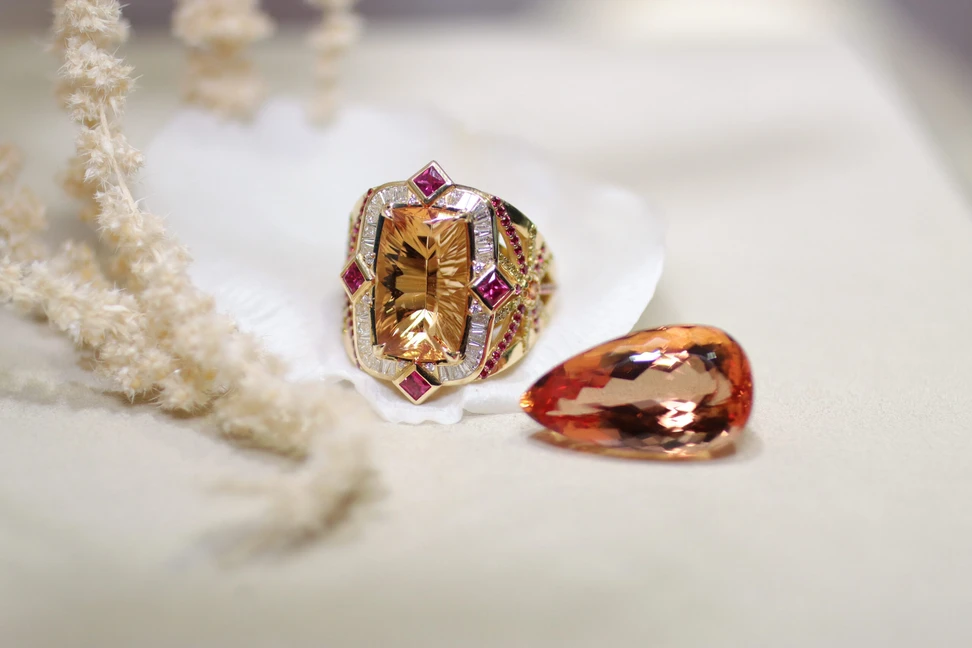 <p>Palm Beach Gems by Nicole Deco Soleil ring, designed by Robin Callahan, set with a fantasy-cut Imperial topaz by Dalan Hargave, surrounded by diamonds and rubies in 18k yellow gold</p>