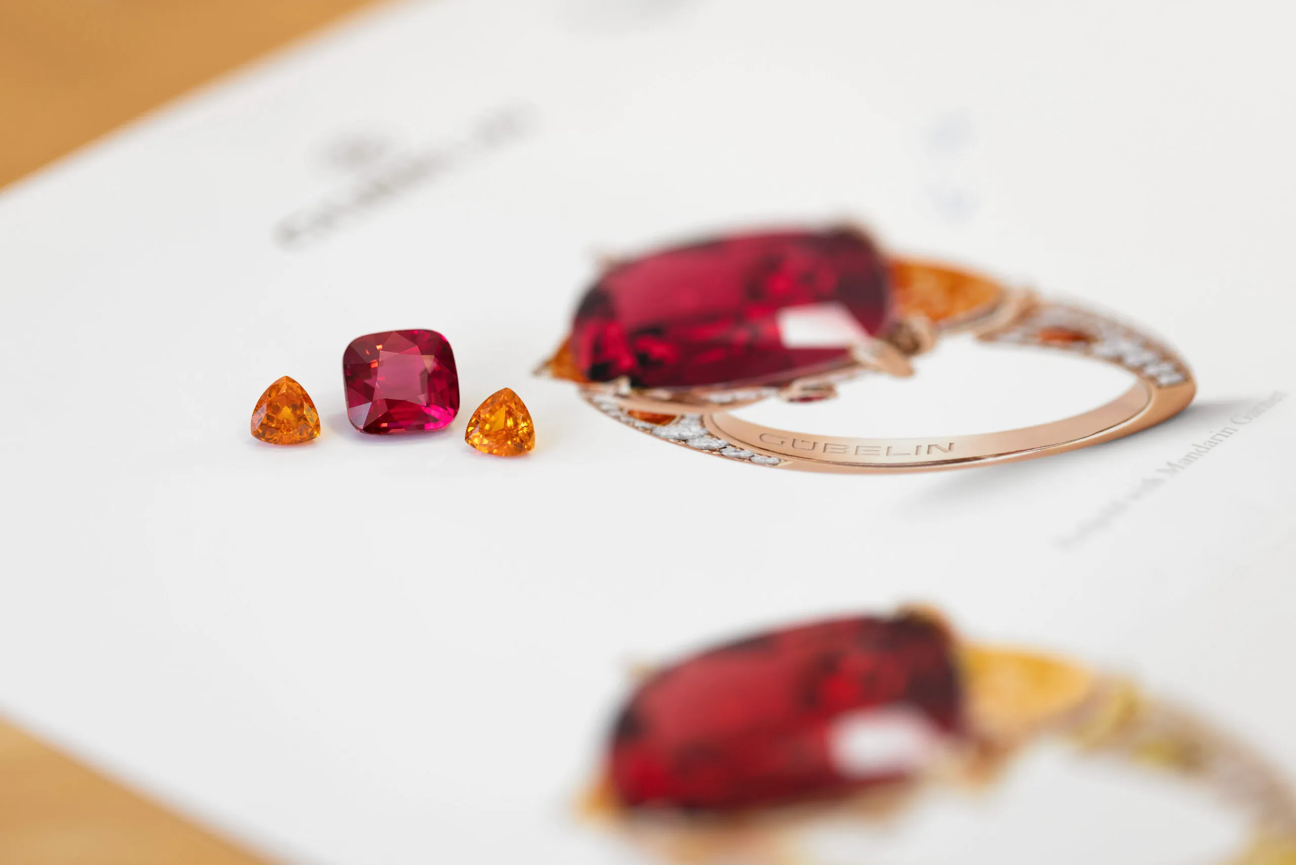 A cushion-shaped Tanzanian purplish-red spinel of more than 9 carats alongside two mandarin garnets. Red and pink spinels were discovered in Tanzania in 2007 and are renowned throughout the world for their colour