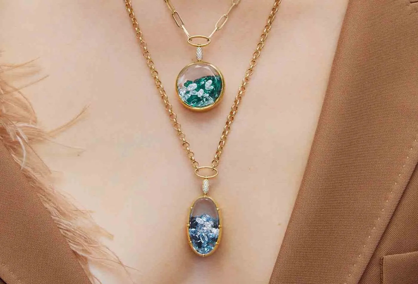 A model wears locket-style pendants from the Aponine Sparks collection with loose gemstones in shades of green and blue