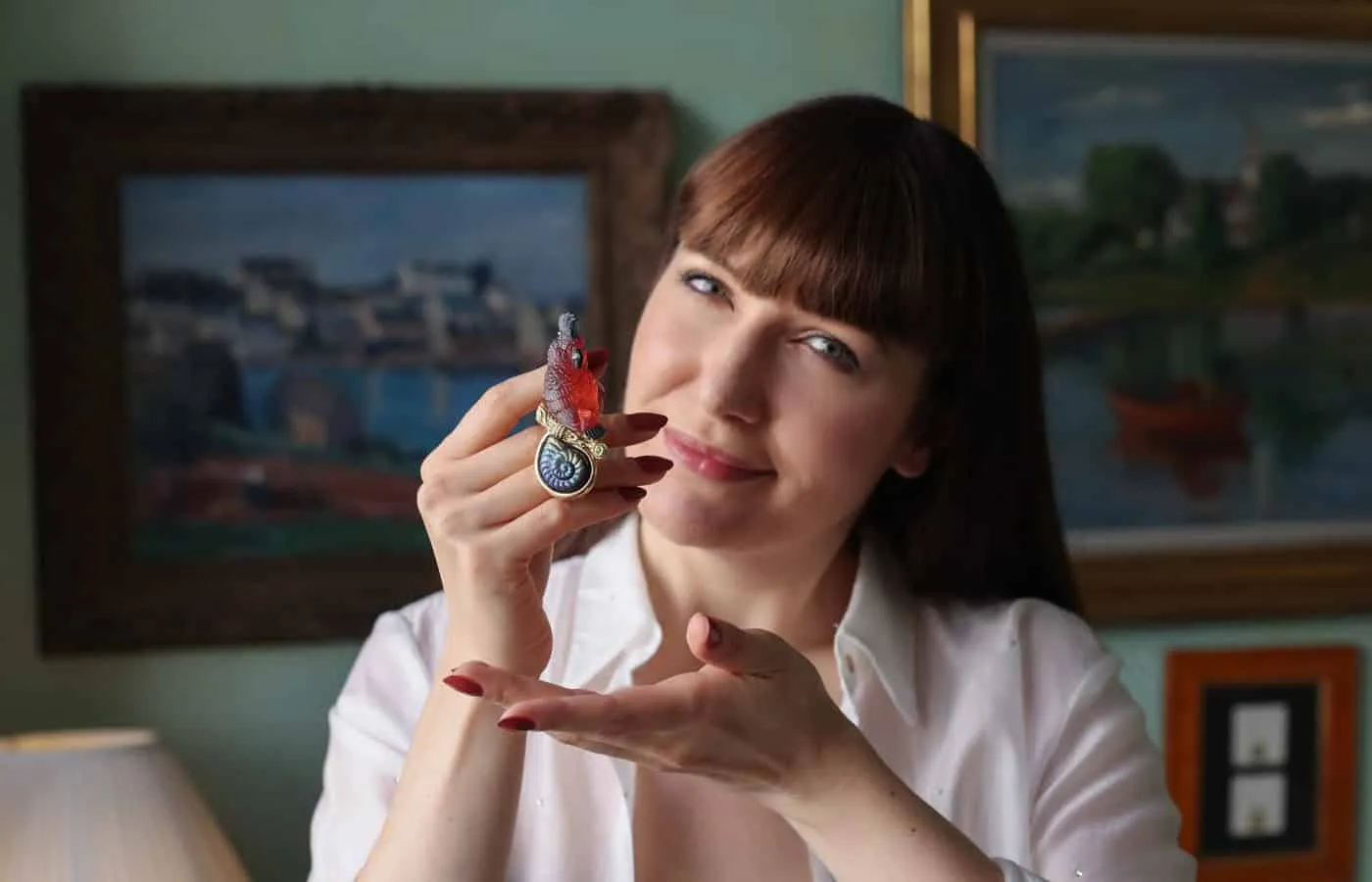 Katerina Perez holds the "Mozart" pin by Elizabeth Gage, crafted with a carved orange-red tourmaline, with quartz eyes and a blue tourmaline plume and tail, totalling 102.13 carats, and a carved spectrolite snail cameo of 27.24 carats, set in 18k yellow gold