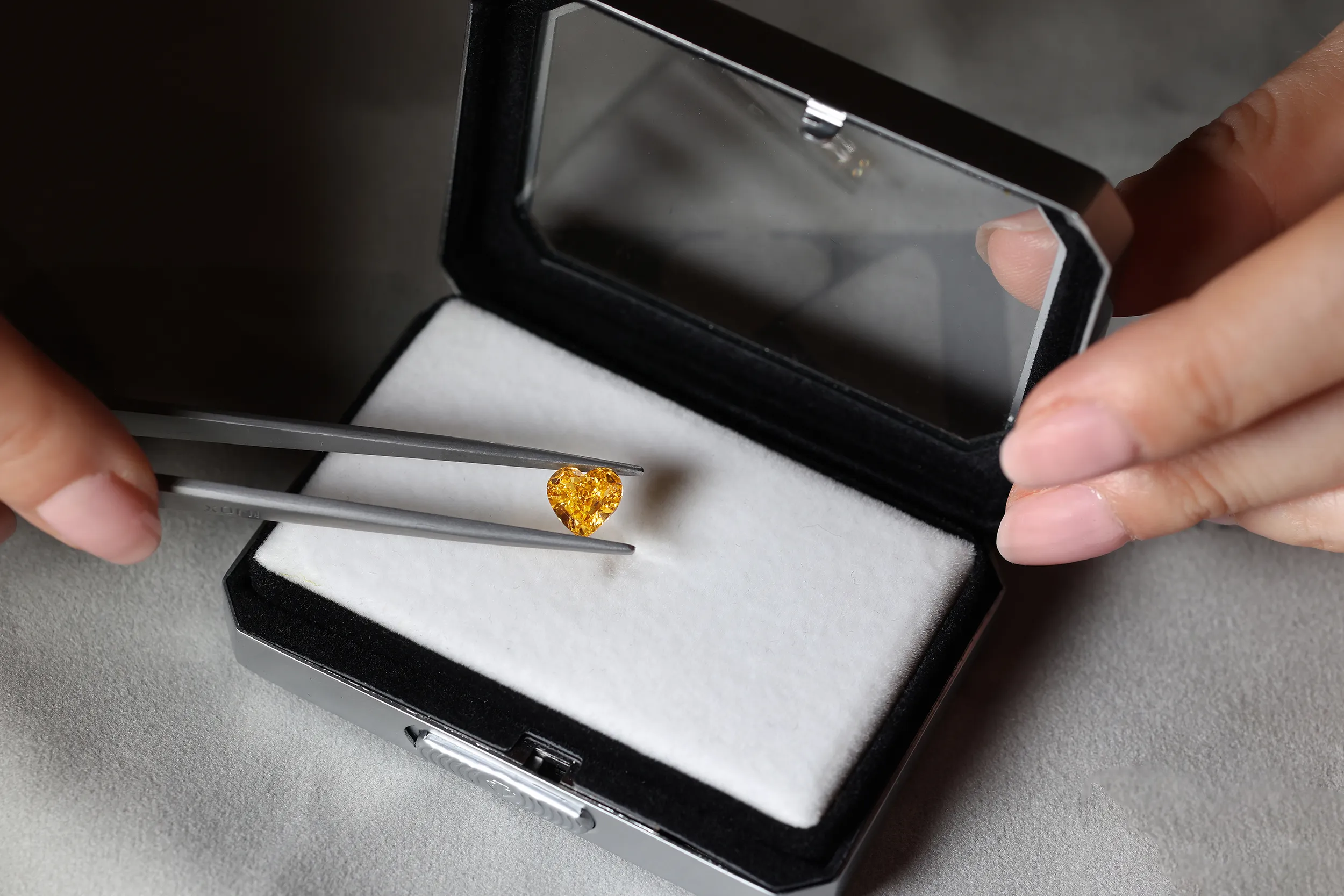 <p>Katerina examines a loose Fancy Vivid Yellow-Orange heart shape diamond</p>