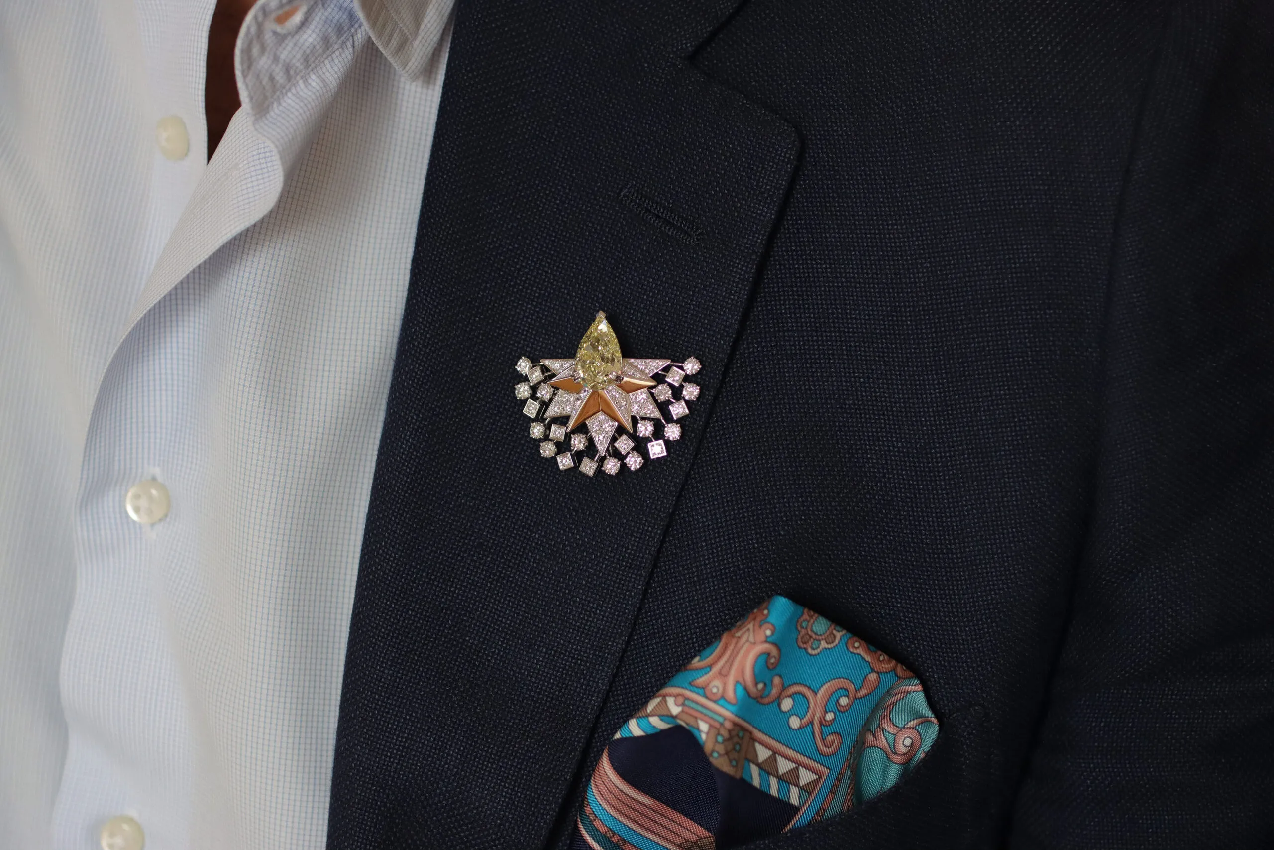 Sahag Arslanian wears the central motif of the Sun Rays High Jewellery necklace as a lapel brooch, set with an 8.88-carat pear-shaped fancy yellow VS2 diamond and surrounded by white diamonds in 18k white and yellow gold 