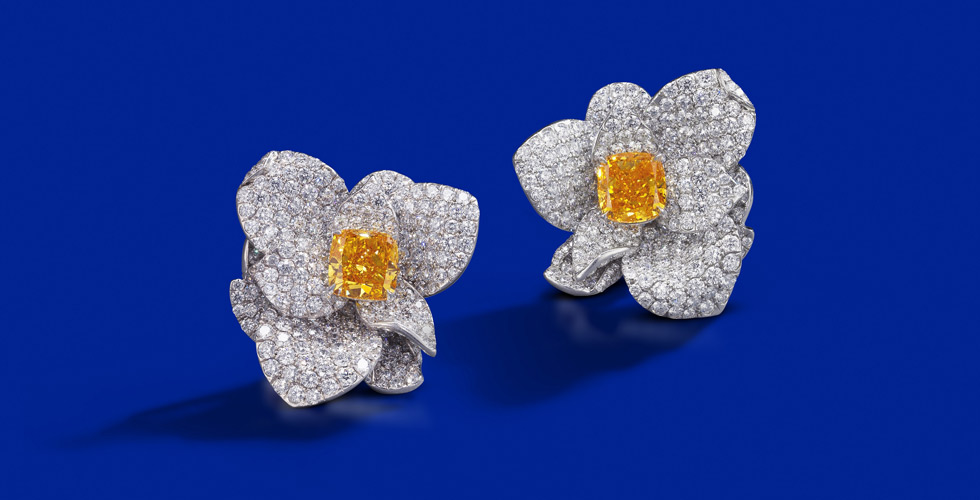 Серьги с редкими цветными бриллиантами. У каждого цветка в центре бриллиант огранки «радиант». Один камень яркого желто-оранжевого цвета весит 2.87 карата, другой 2.53 карата. Предполагаемая цена: $ 360,00 — $ 490,000
