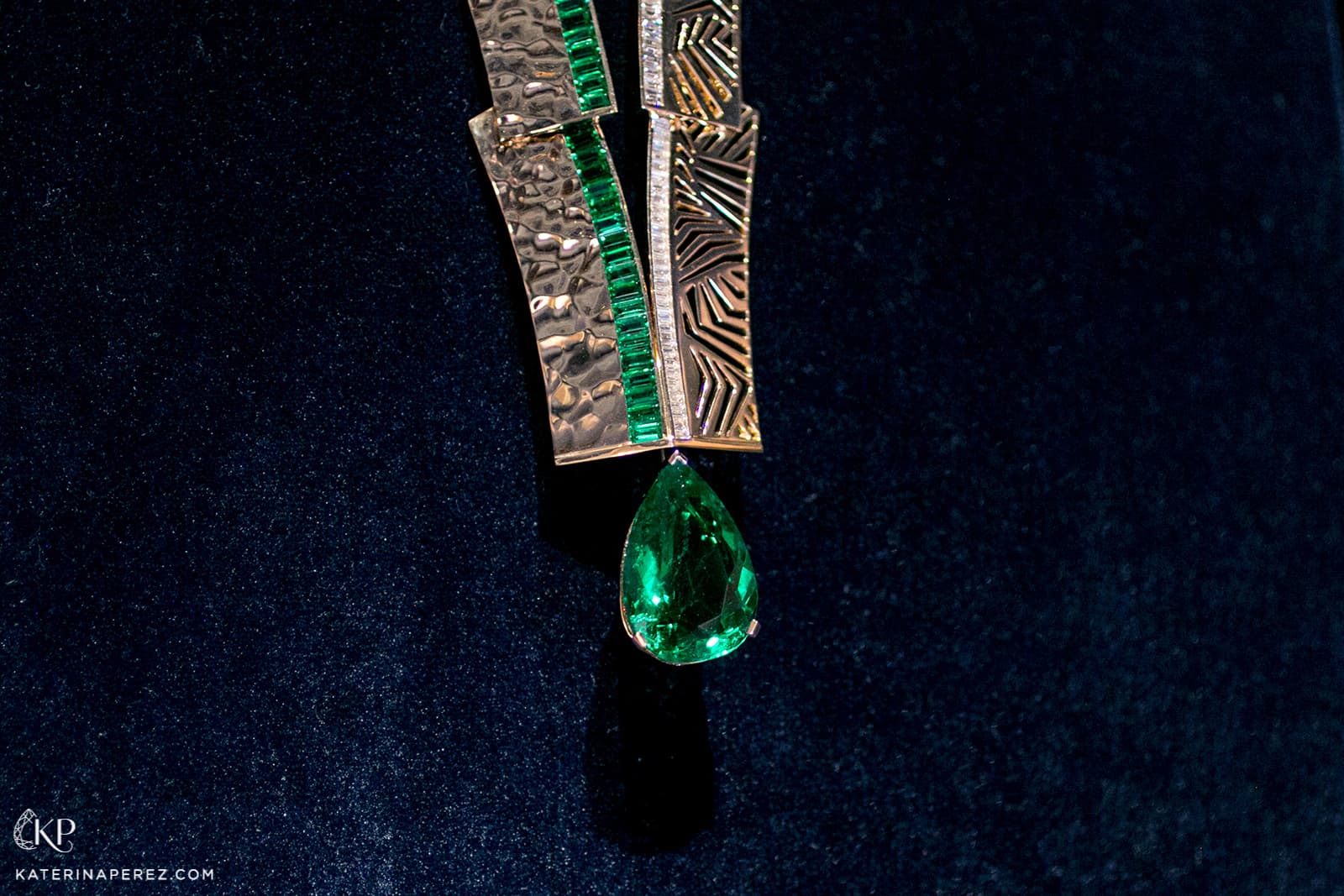  Crafted in textured yellow gold, suspended beneath is a vivid green 16.06 carat pear-shape Colombian emerald