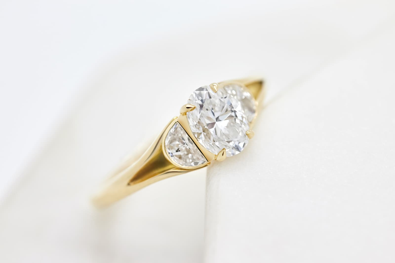 Taylor & Hart trilogy engagement ring with oval diamond centre flanked with half moon diamonds in yellow gold