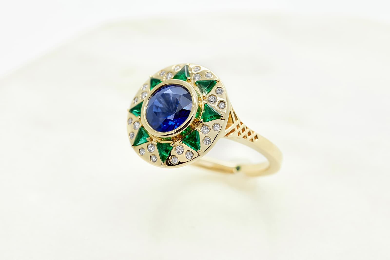  A blue sapphire sun-inspired engagement ring set in yellow gold with custom cut emeralds and round diamonds by Taylor & Hart