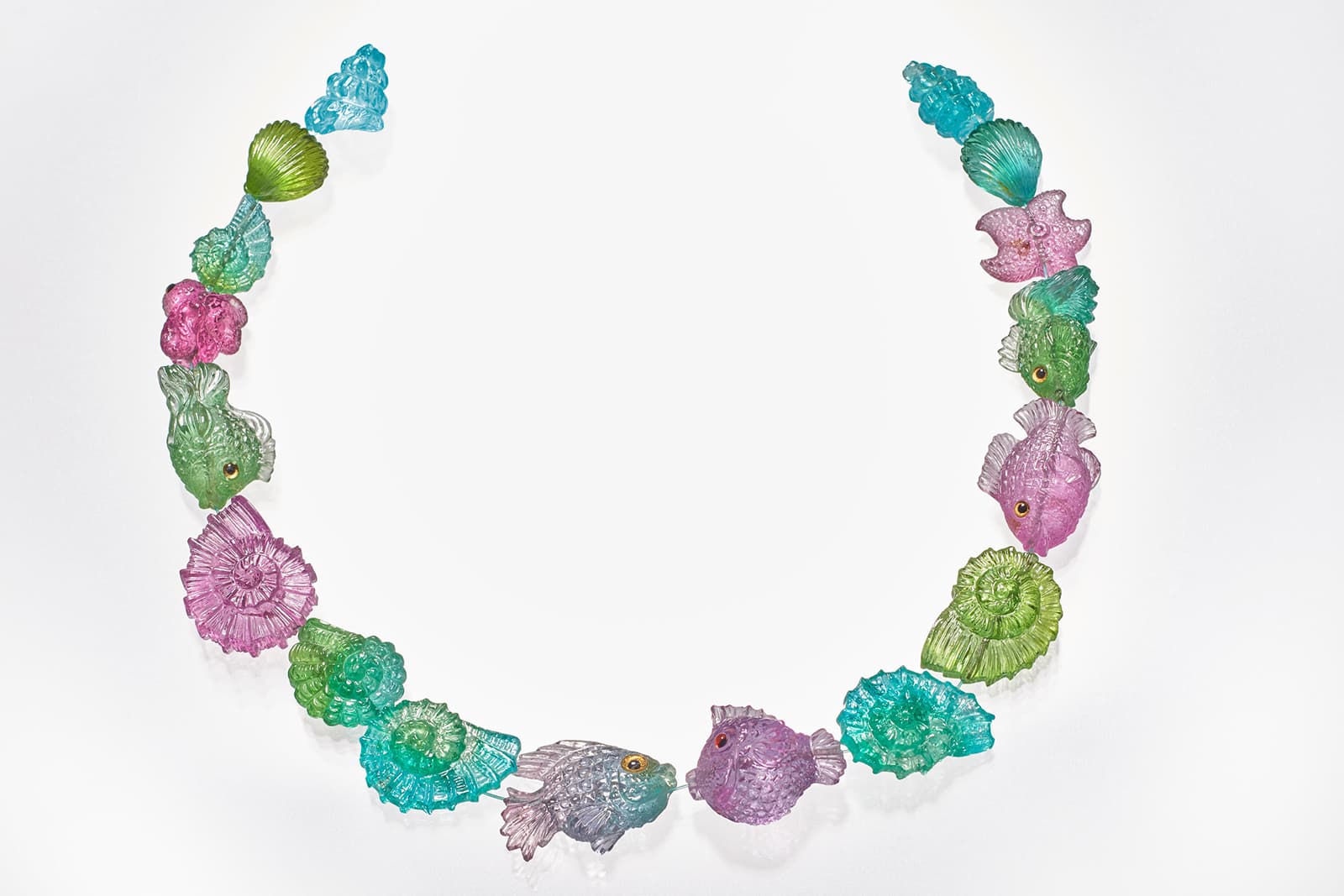 A fish and seashell inspired carved gemstone necklace layout by Paul Wild, including Paraiba tourmaline