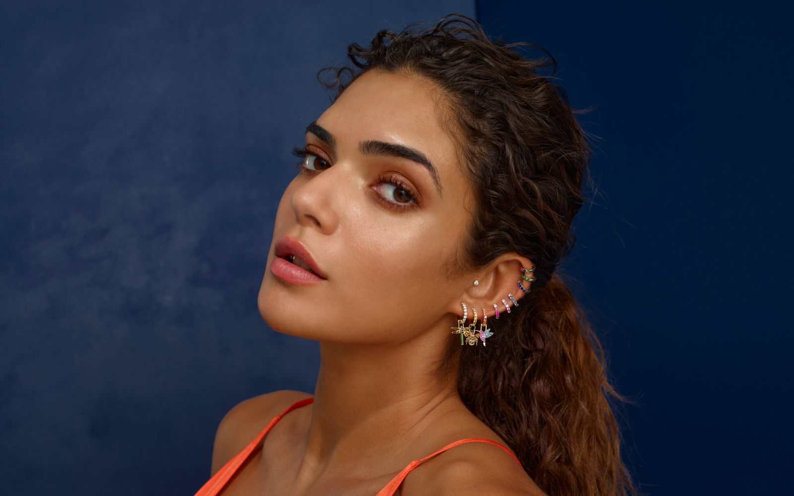 A model wears Robinson Pelham Orb Hoop earrings and EarWish charms with coloured gemstones and diamonds