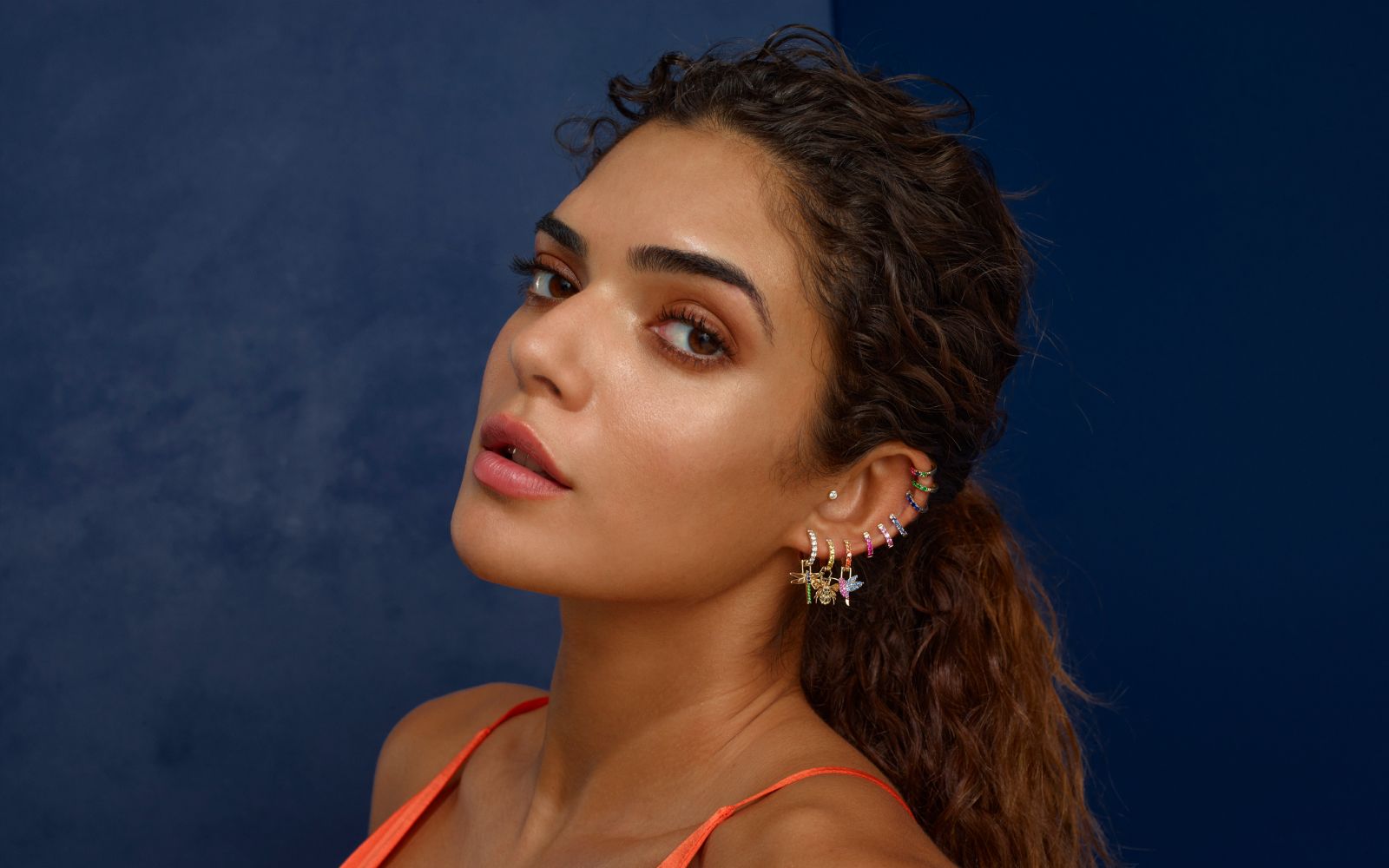 <p>A model wears Robinson Pelham Orb Hoop earrings and EarWish charms with coloured gemstones and diamonds</p>