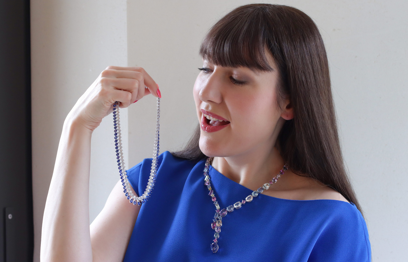Katerina Perez holding a selection of Bucherer Fine Jewellery necklaces featuring diamonds and multicoloured sapphires