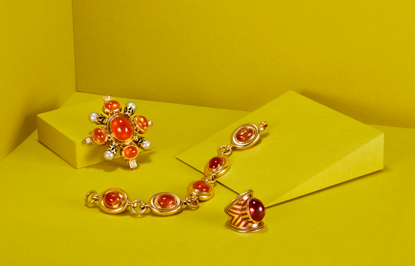  Elizabeth Gage Mandarin Garnet Kiss pin in gold, enamel, mandarin garnet, pearl and diamond, the Sunstone bracelet in gold and sunstone, and the  Mandarin Garnet Tapered Templar Ring  in gold, enamel and mandarin garnet