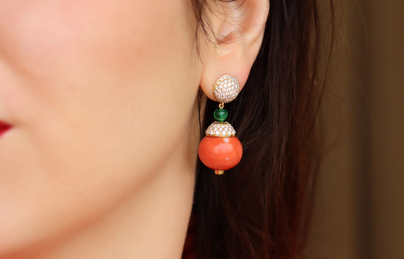  Katerina Perez wears a pair of Veschetti earrings with round coral drops, emeralds and diamonds in gold