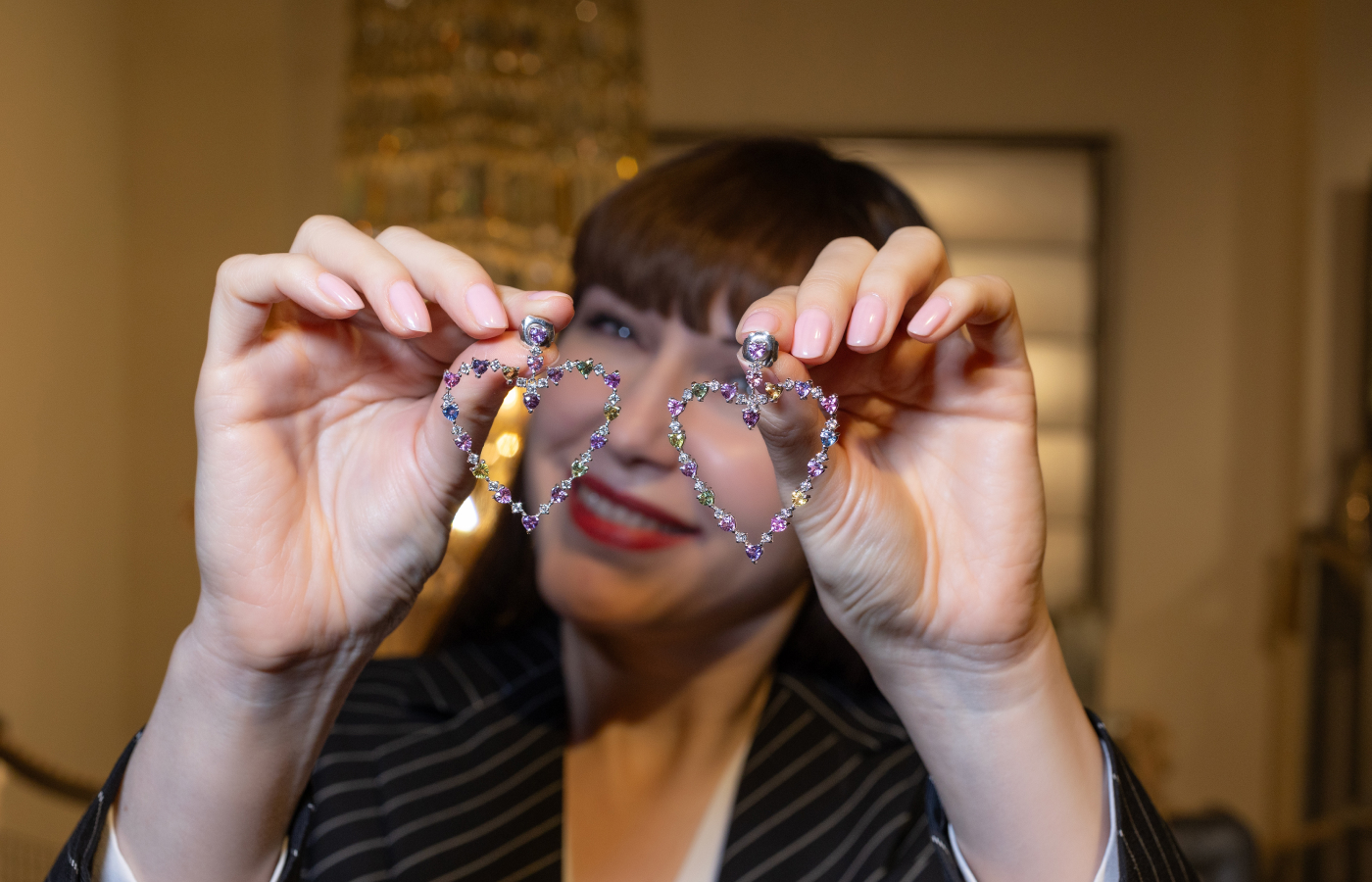  Katerina Perez holds a pair of heart-shaped multi-coloured gemstone earrings by ZARIG