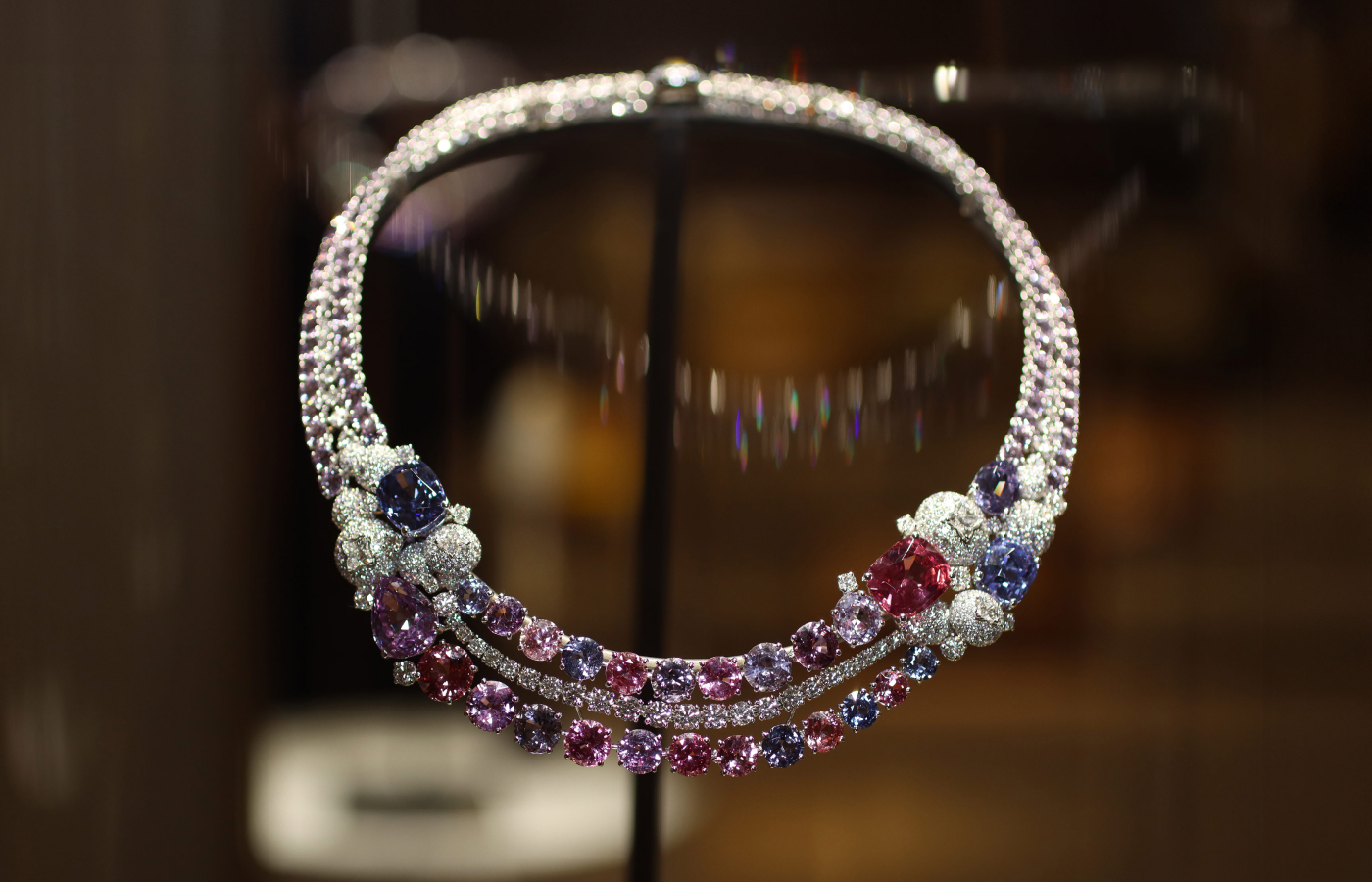 A photograph of the Symbiosis necklace in 18k white gold with two pear-cut purple spinels of 4.13 carats and 10.11 carats, one cushion-cut pink spinel of 10.03 carats, one cushion-cut purple spinel of 8.46 carats, one cushion-cut blue spinel of 10.67 carats and four LV Monogram Star-cut diamonds for 1.89 carats, plus further spinels and diamonds, part of the Louis Vuitton Deep Time Chapter II High Jewellery collection