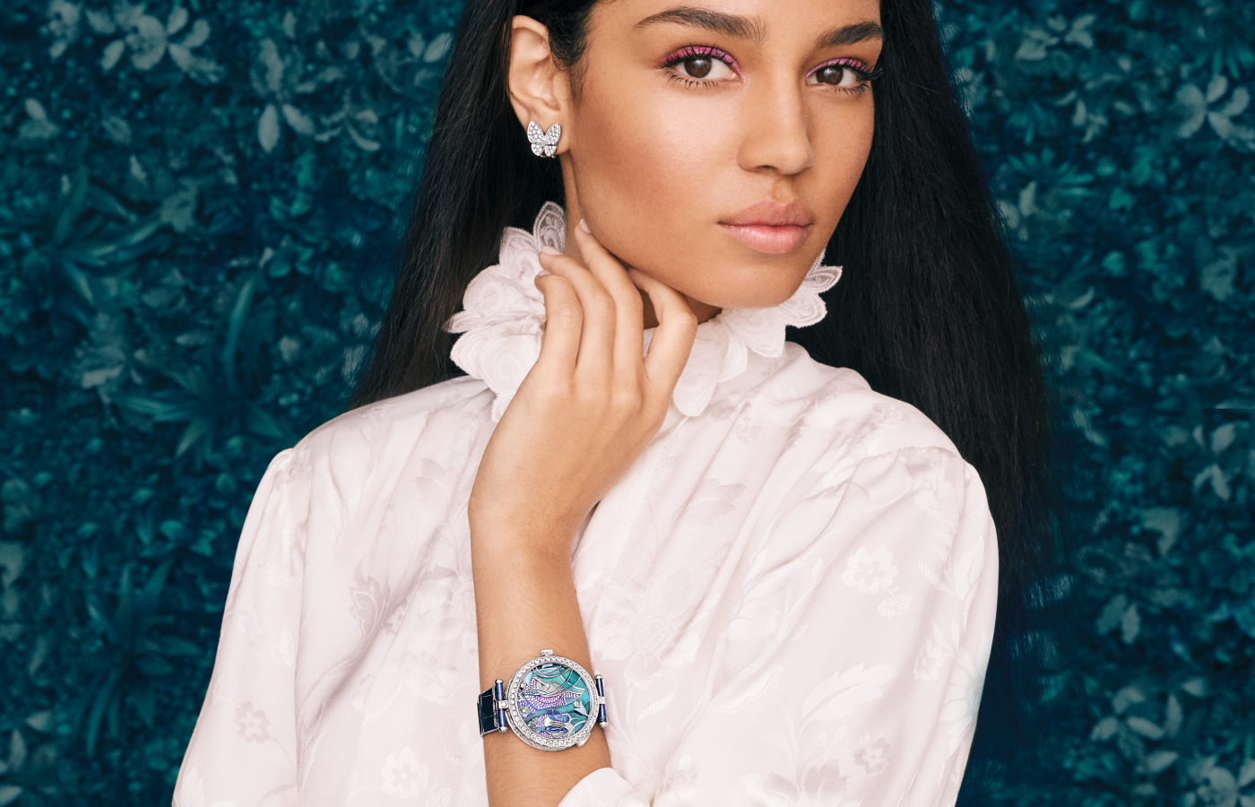 A model wears the Van Cleef & Arpels Lady Arpels Papillon Automate watch with a 40mm diamond-set case in white gold, featuring blue, mauve and purple sapphires, mother of pearl, champlevé, paillonné and plique-à-jour enamel, and miniature painting