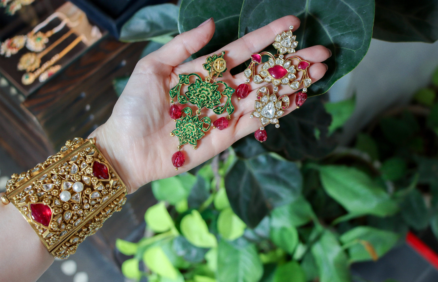 Katerina Perez wearing an Amrapali bangle and holding a pair of earrings in gold set with pearls, rubies, spinels, polki diamonds and diamonds