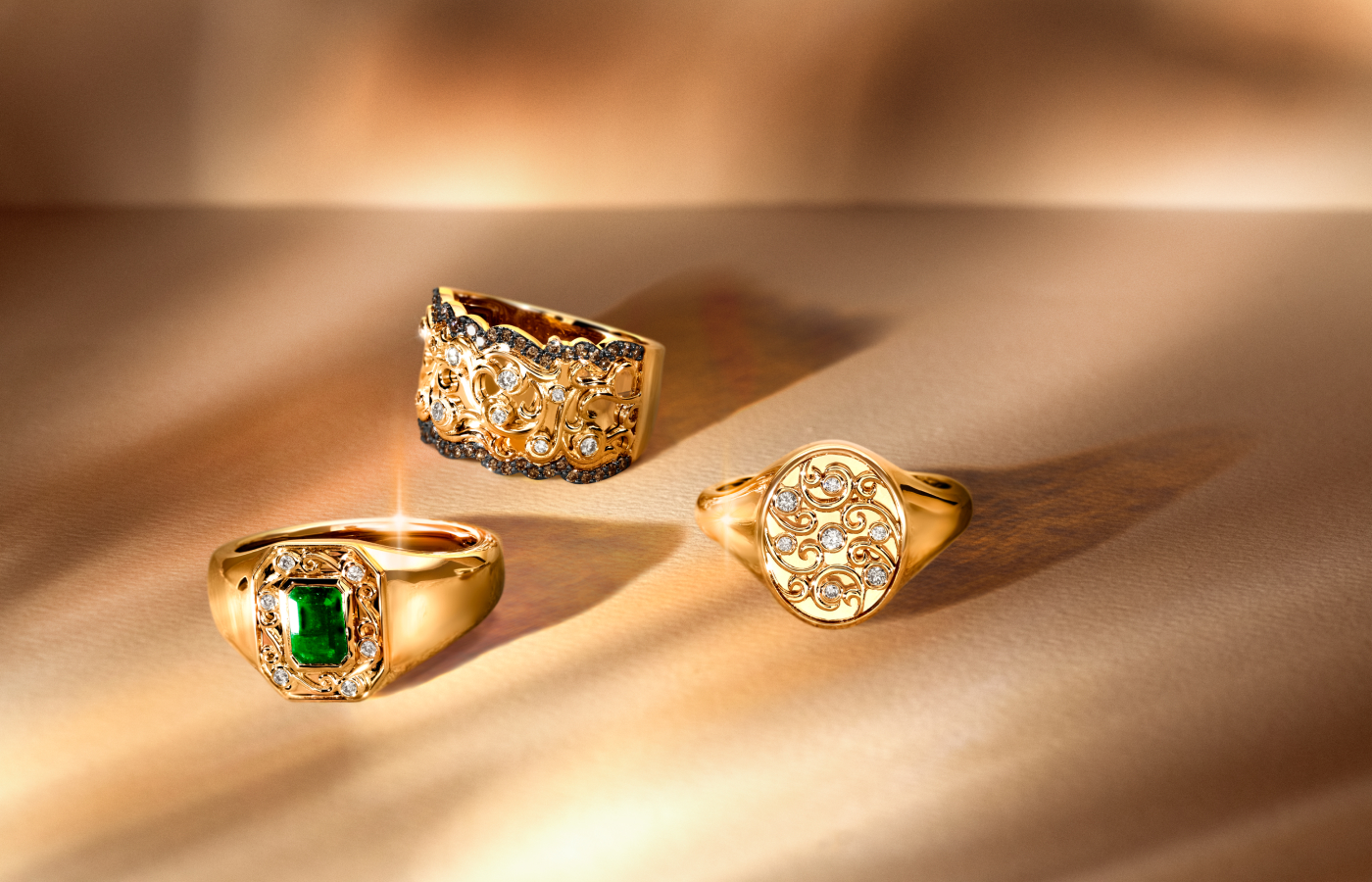 Clockwise from top: Le Vian® ring with Nude Diamonds™ and Chocolate Diamonds® set in 14K Honey Gold™, Le Vian® ring with Nude Diamonds™ set in 14K Honey Gold™, and a third Le Vian® ring with a 0.75 carat Costa Smeralda Emeralds™ gemstone and Nude Diamonds™, also set in 14K Honey Gold™