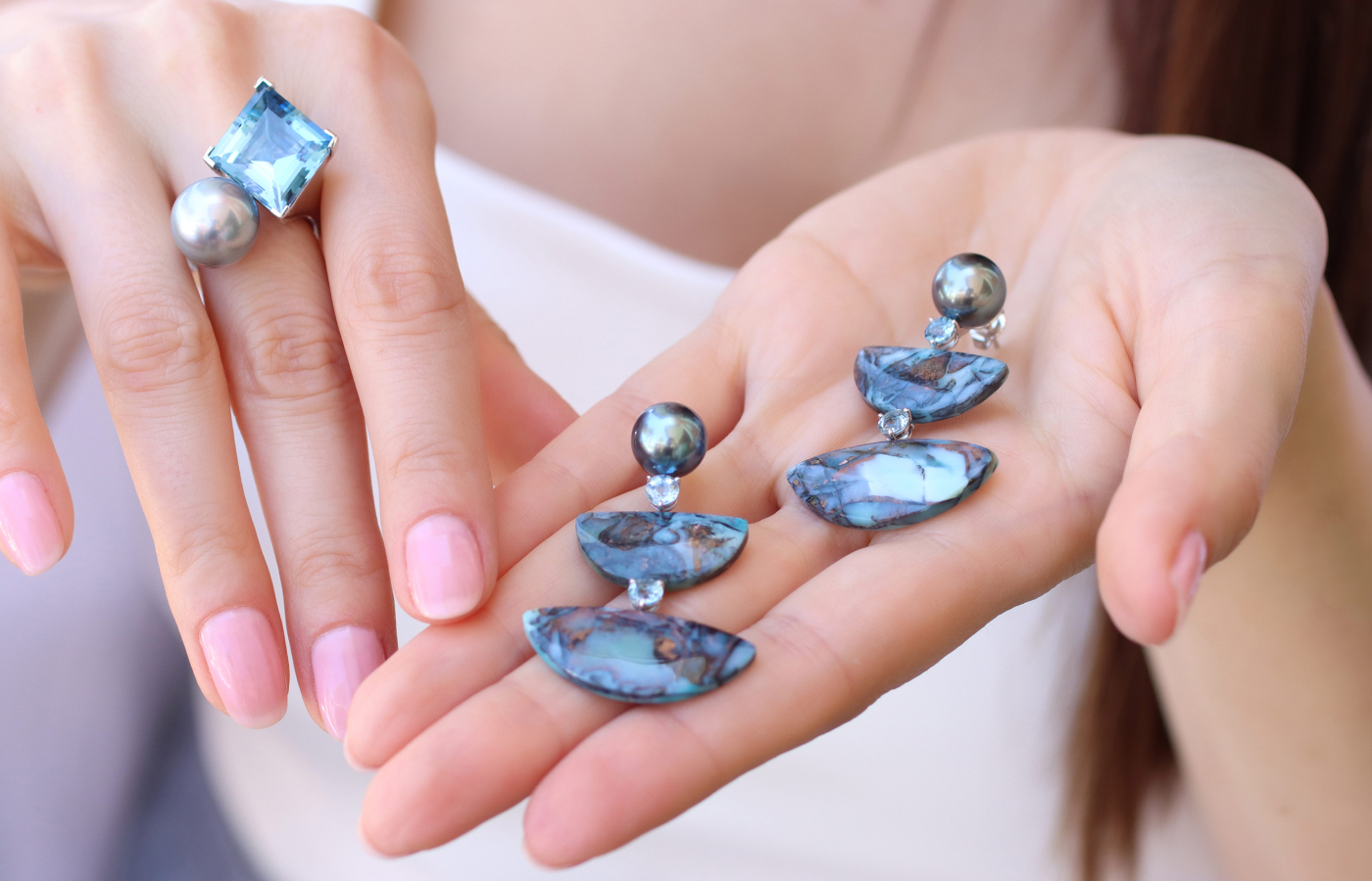  Katerina Perez wears an Assael ring with a 10.45 carat kite-shaped Brazilian aquamarine and a Tahitian pearl while holding a pair of Assael earrings featuring opalised fossil wood with native copper, aquamarine and Tahitian cultured pearls