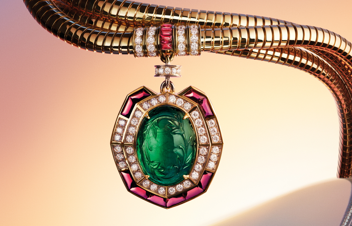 Close up of the Bvlgari Tubogas of Time necklace from the Aeterna collection with a striking oval-cut 31.07-carat Zambian emerald and buff-top rubellites and pavé-set diamonds in 18k yellow gold