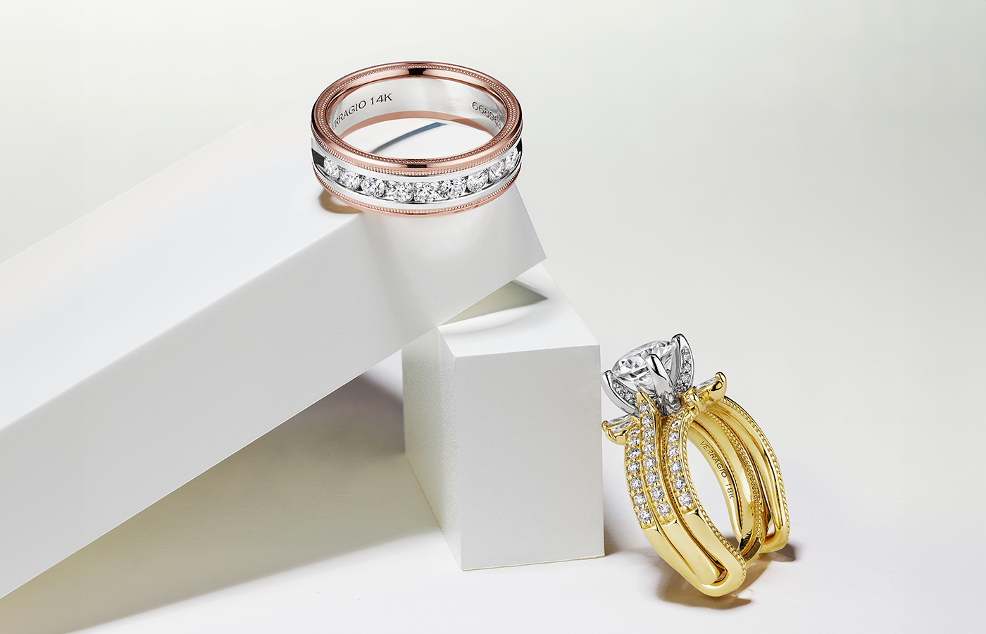  Vanguard Embellisher™️ from the Verragio Vanguard collection with an oval-shaped diamond engagement ring, both in 14k yellow gold, alongside a men’s band with diamonds in 18k rose gold 