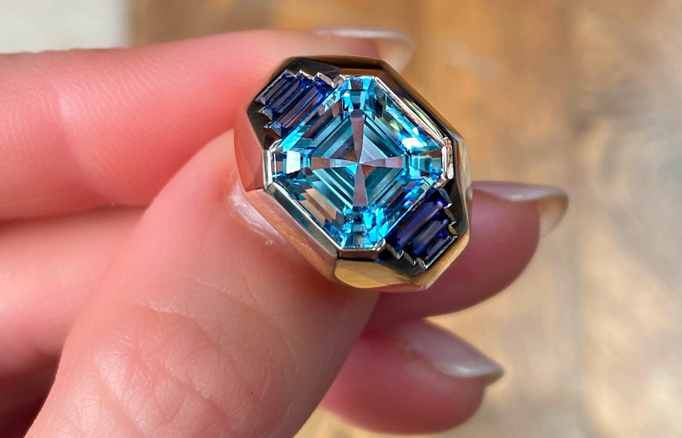  A close up of Hattie Rickards’ bespoke engagement ring for Portia, crafted with a custom-cut octagonal aquamarine and blue sapphire baguettes, set in yellow and white gold